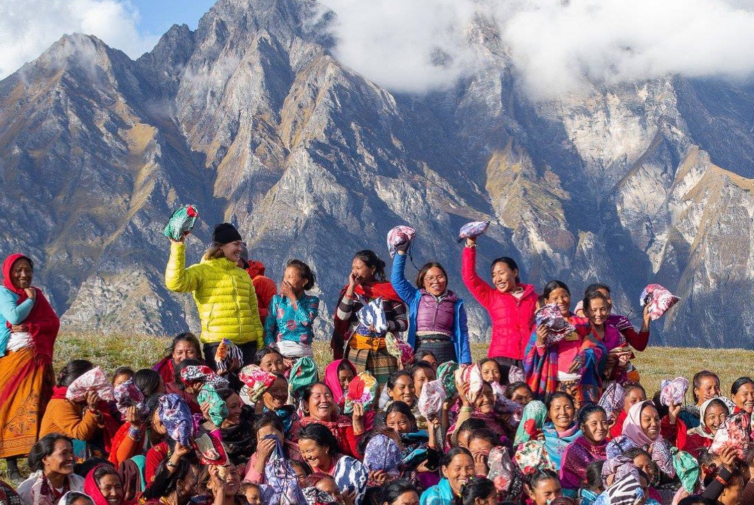 large group of females on a grassy area with mountains and clouds behind them