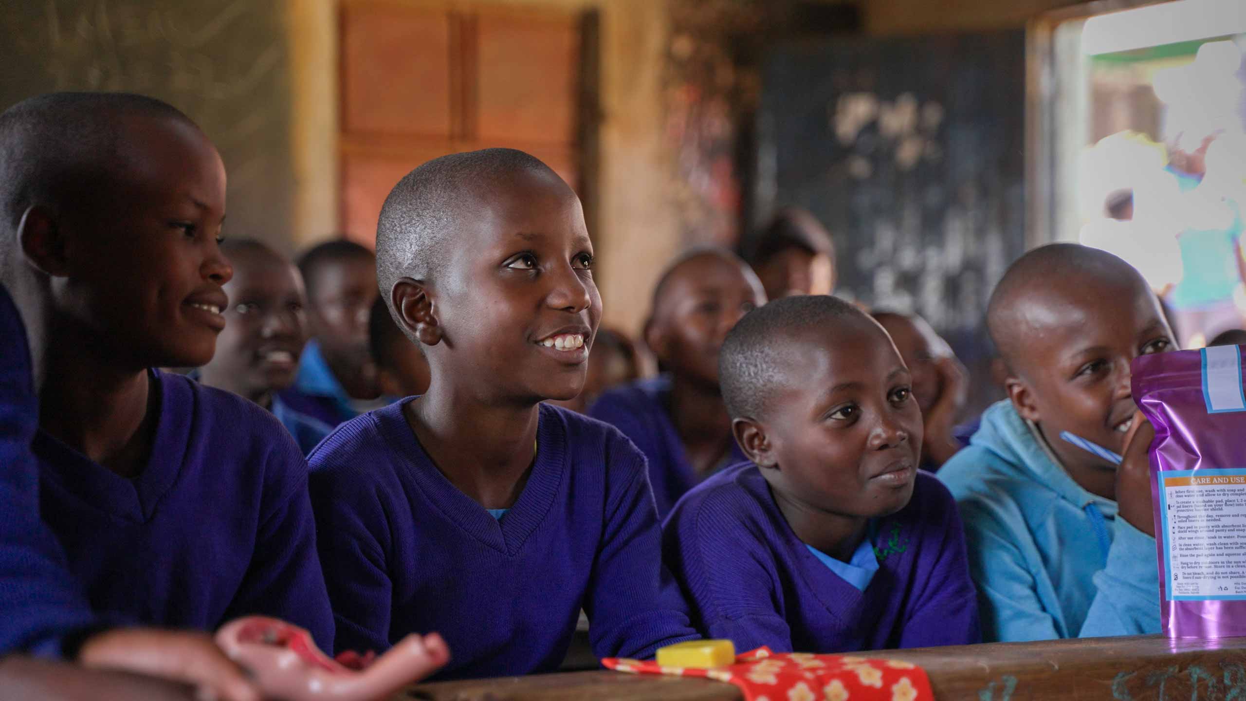 four young Kenyan children are listening to a presentation with smiling faces