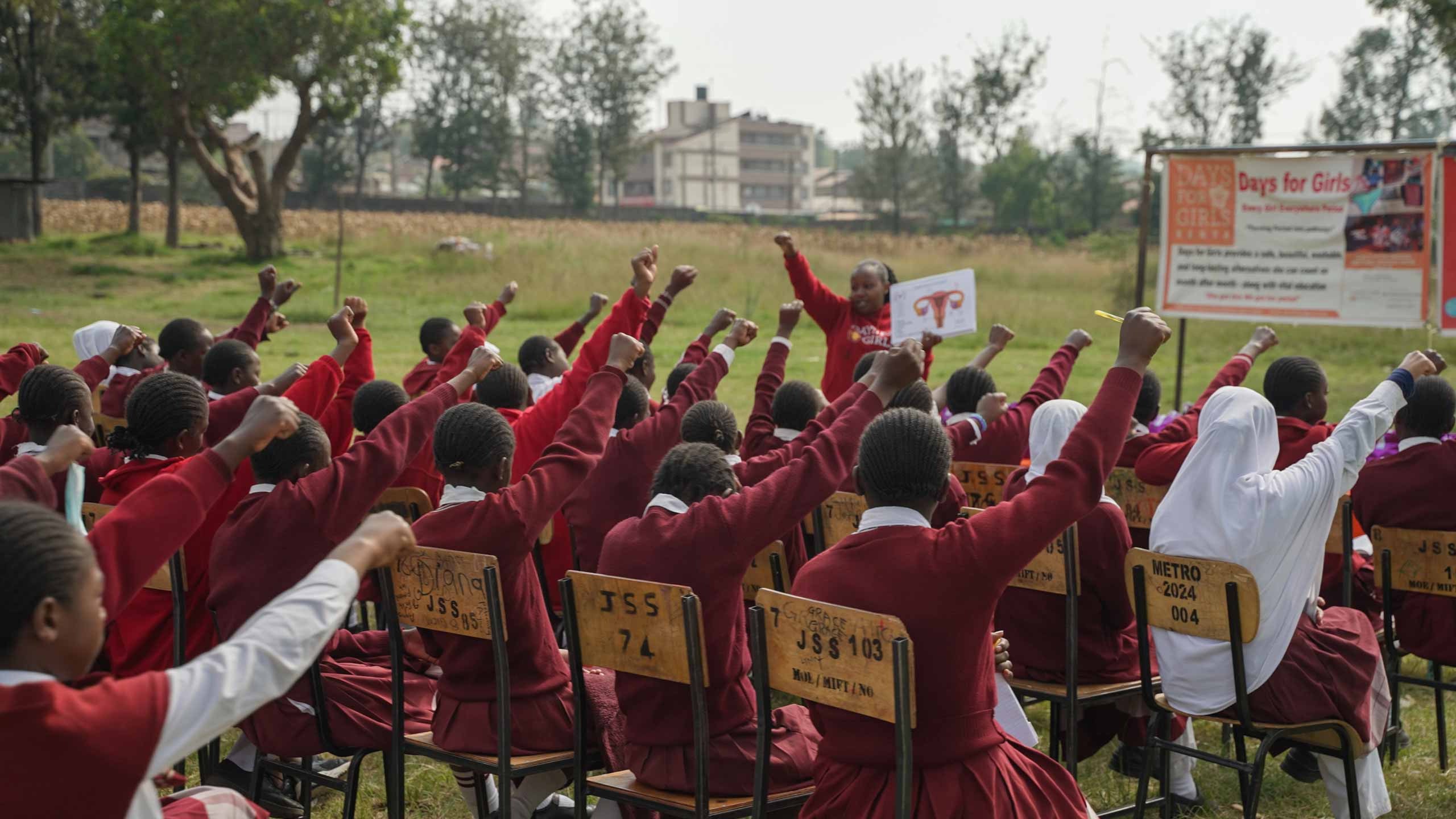 the view from the back of an outdoor Days for Girls presentation in Kenya with rows of young women raising their arms