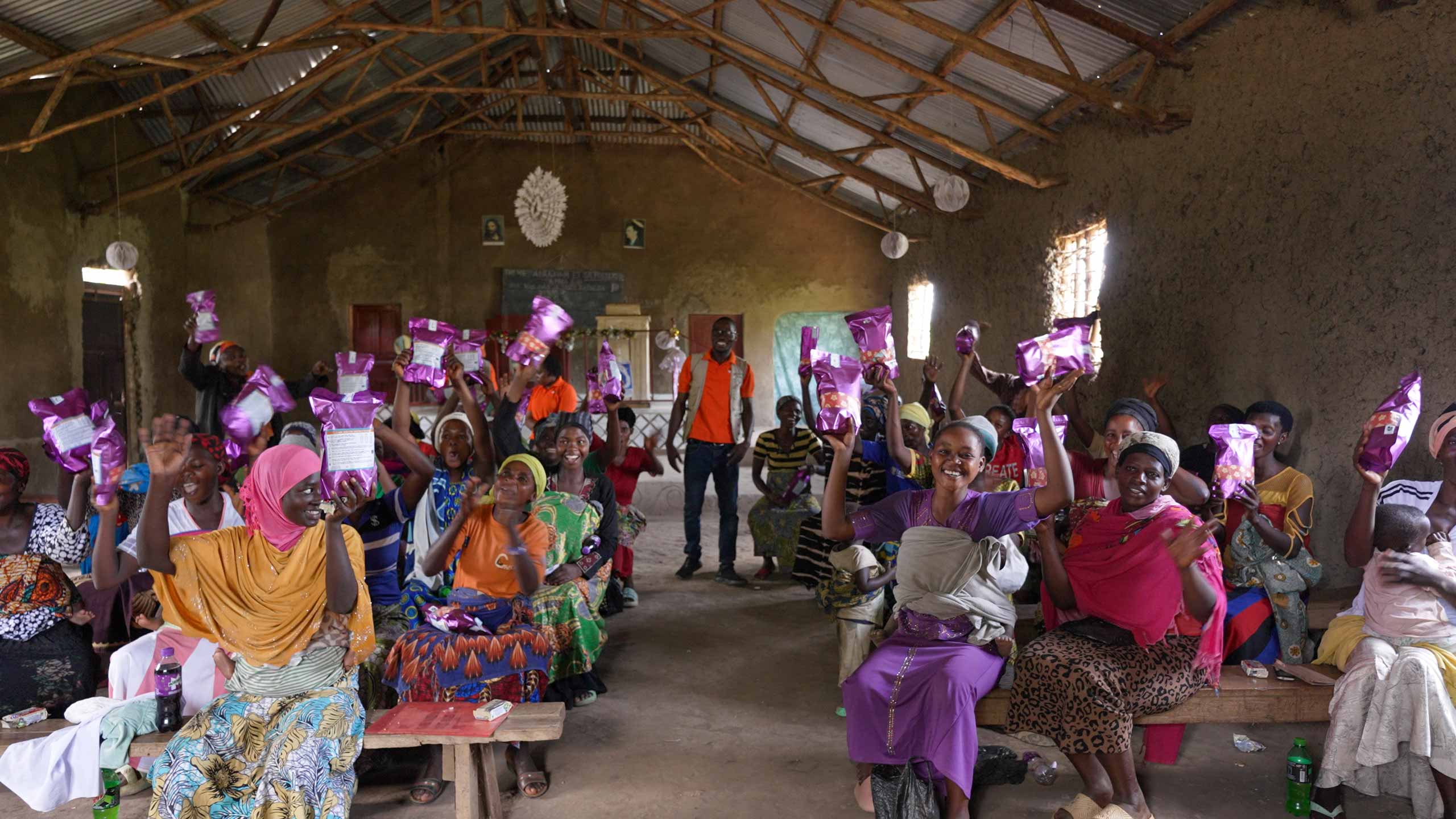a group of Ugandan women seated on benches holding up Days for Girls period kits
