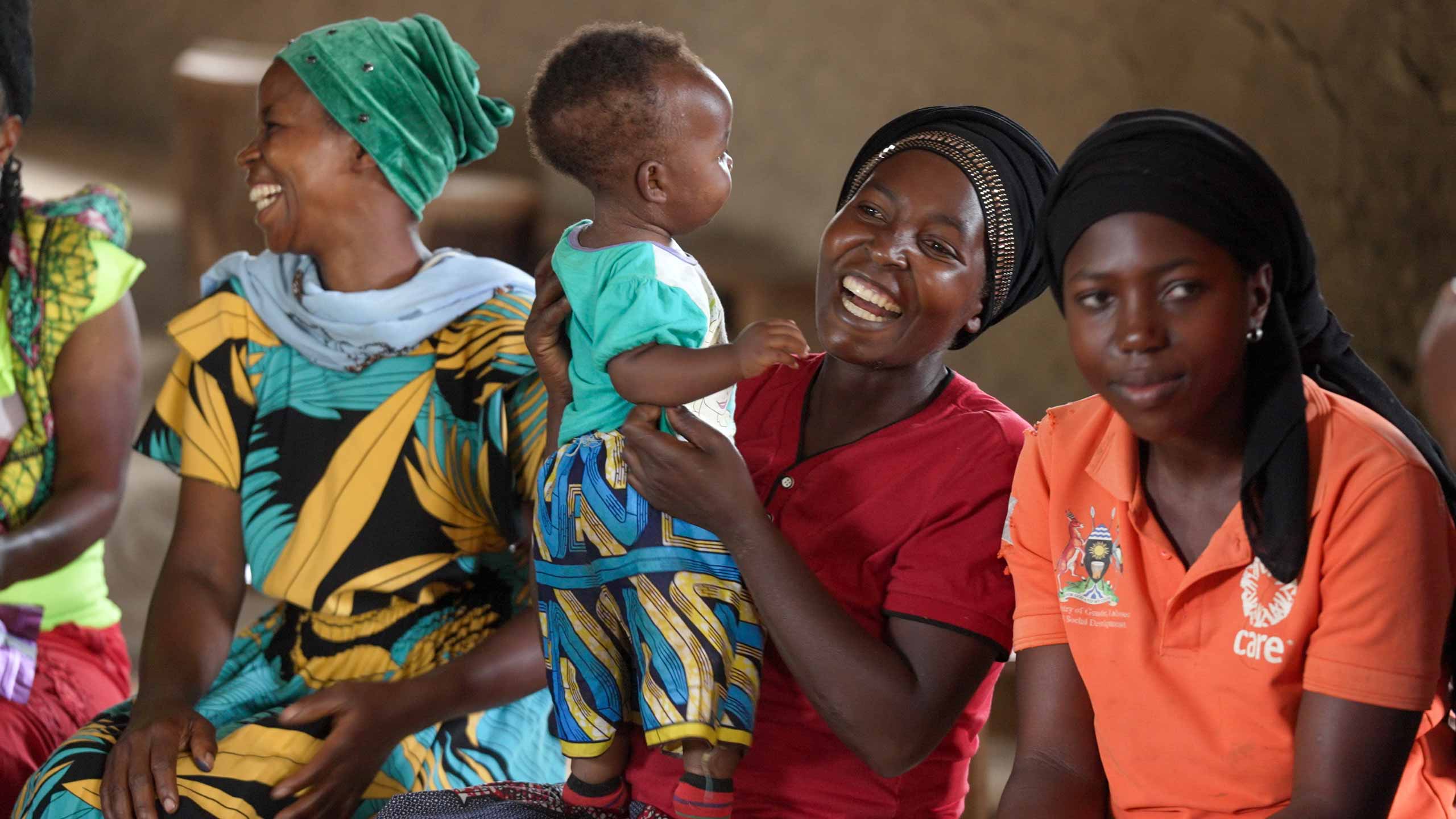 three women seated with the focus on the middle woman who is smiling while holding a toddler